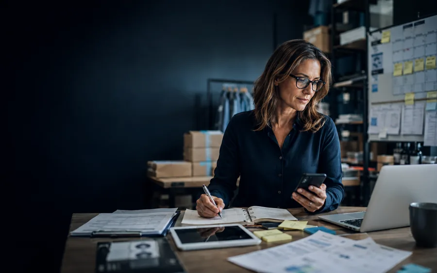 A small-business owner coordinating notes, customer communication, planning and operational work at a desk.